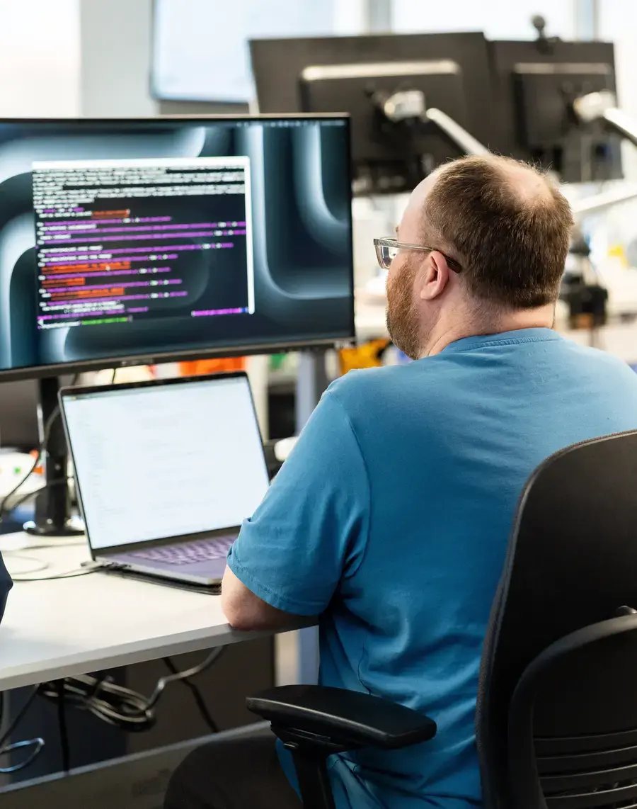 Man working at a desk reviewing code on a computer monitor in an office