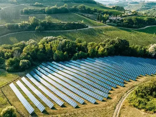 Solar panel array installed on a hillside surrounded by farmland and trees
