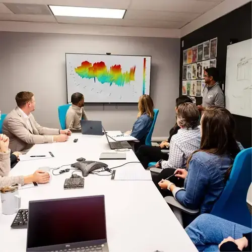Team meeting in a conference room with a presenter showing a colorful data visualization on a large screen