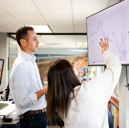 Two colleagues discussing data on a screen in an office meeting