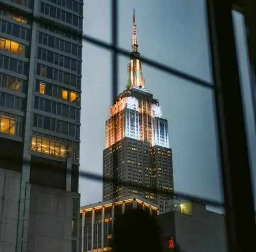 Empire State Building illuminated at night, viewed between nearby buildings