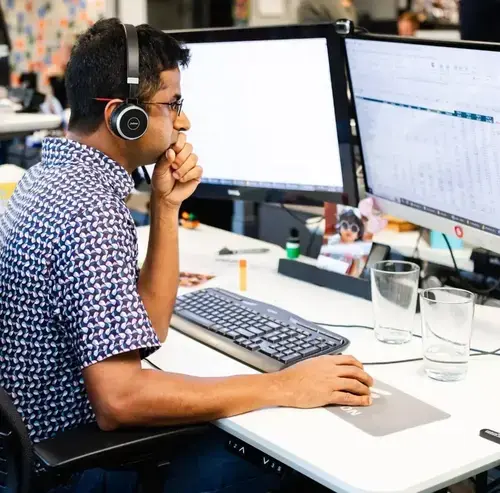 Employee wearing headphones reviewing data on dual computer monitors at an office desk
