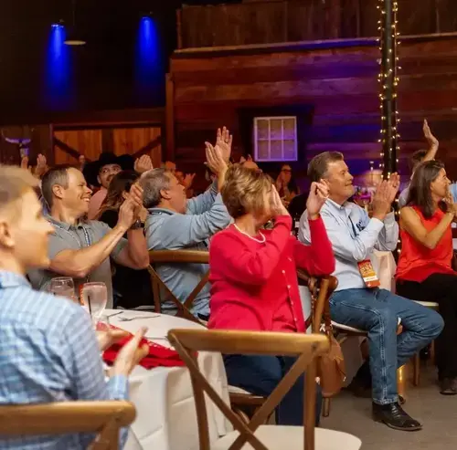 Audience members seated at tables clapping during a presentation at an indoor event